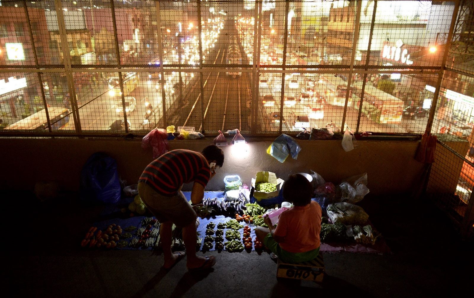 Un vendedor de verduras habla con un cliente en un paso a desnivel en Manila.