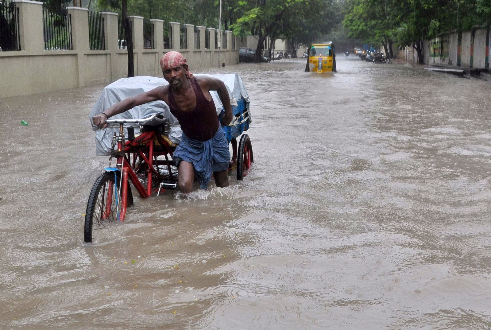 Un trabajador indio empuja su trishaw por las inundaciones en Chennai.