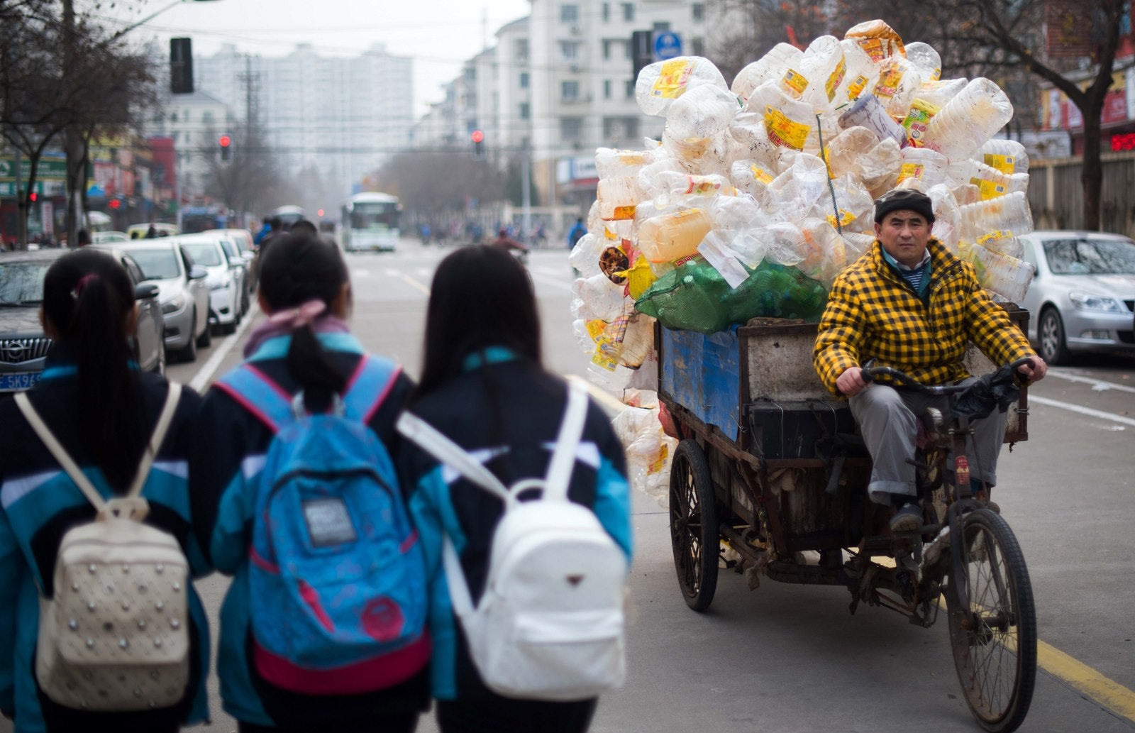 Un hombre monta su triciclo cargado junto a tres colegialas en Shanghai.