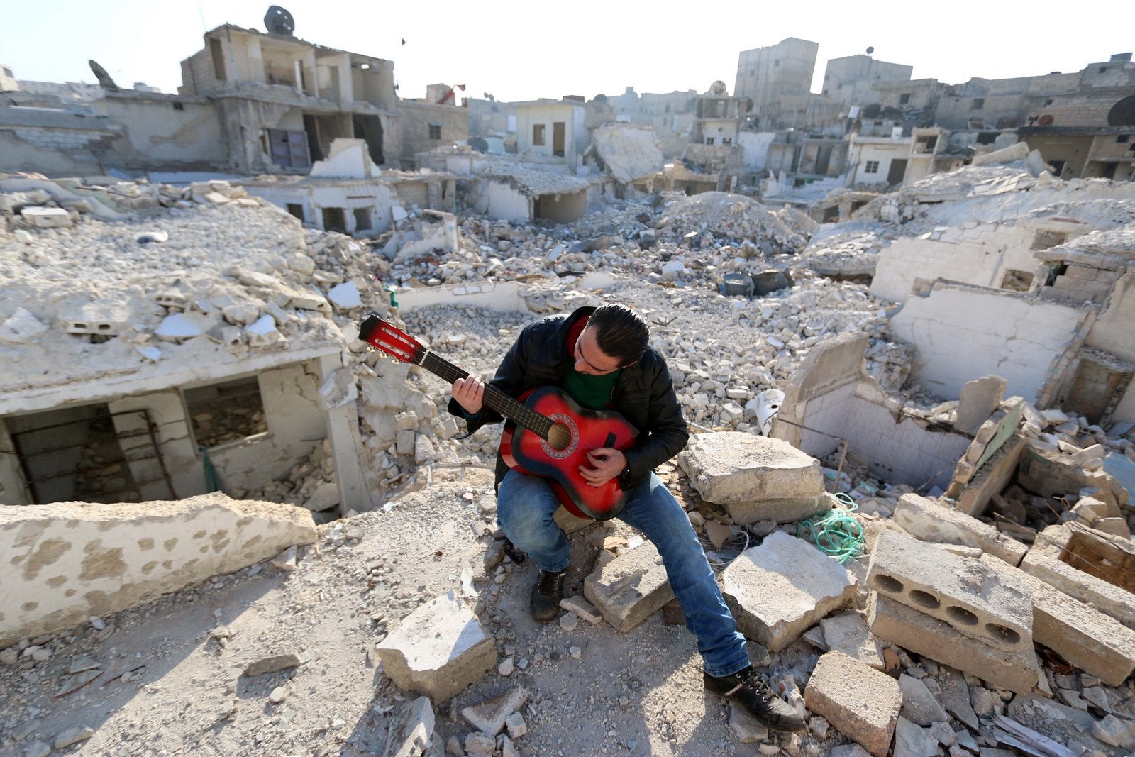Shehab, un sirio de 23 años de edad, toca la guitarra en medio de los escombros de los edificios en la ciudad norteña siria de Alepo.