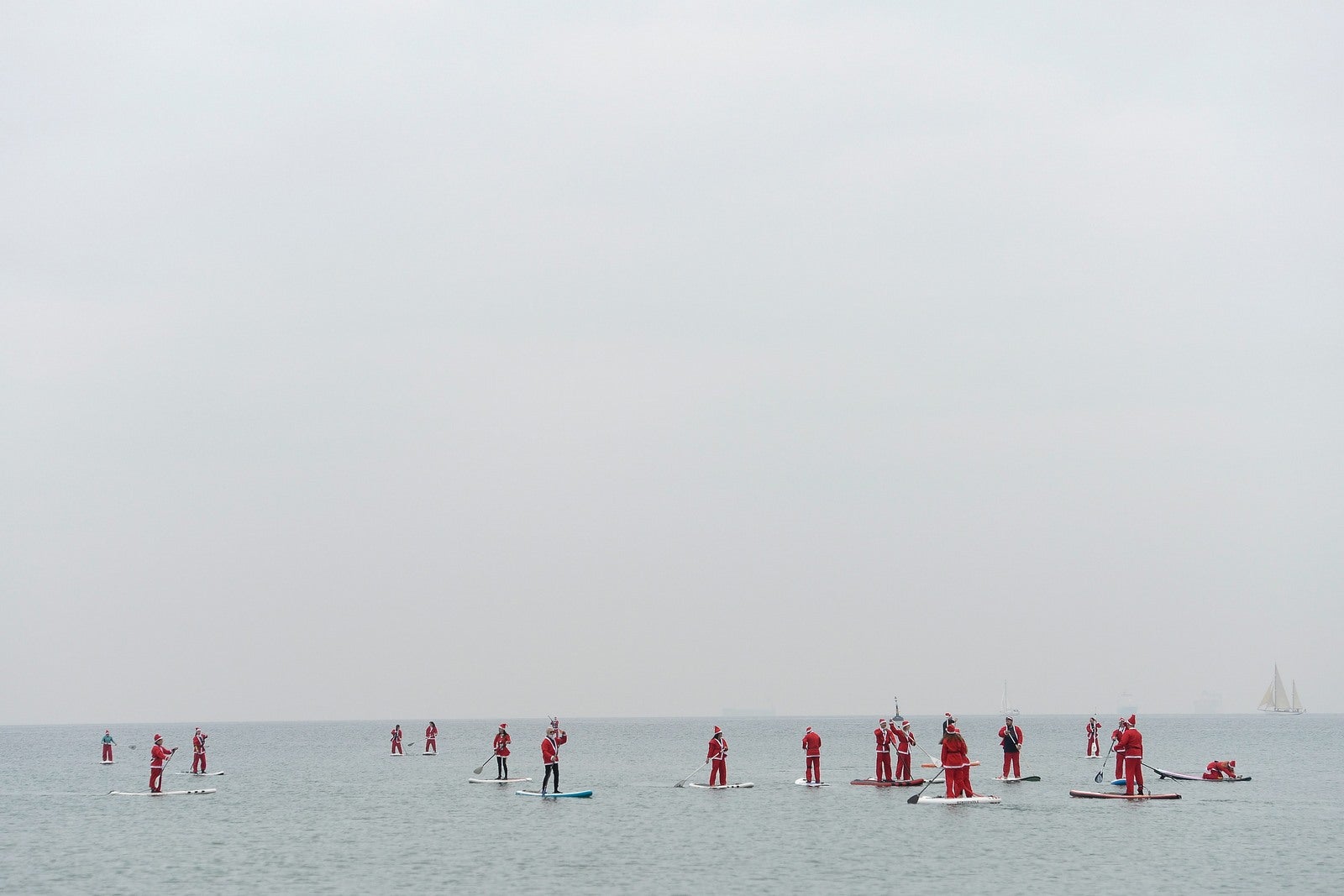 Gente vestida como Santa Claus de pie en tablas de paddle mientras participan en una recaudación de fondos de la playa de Barcelon.
