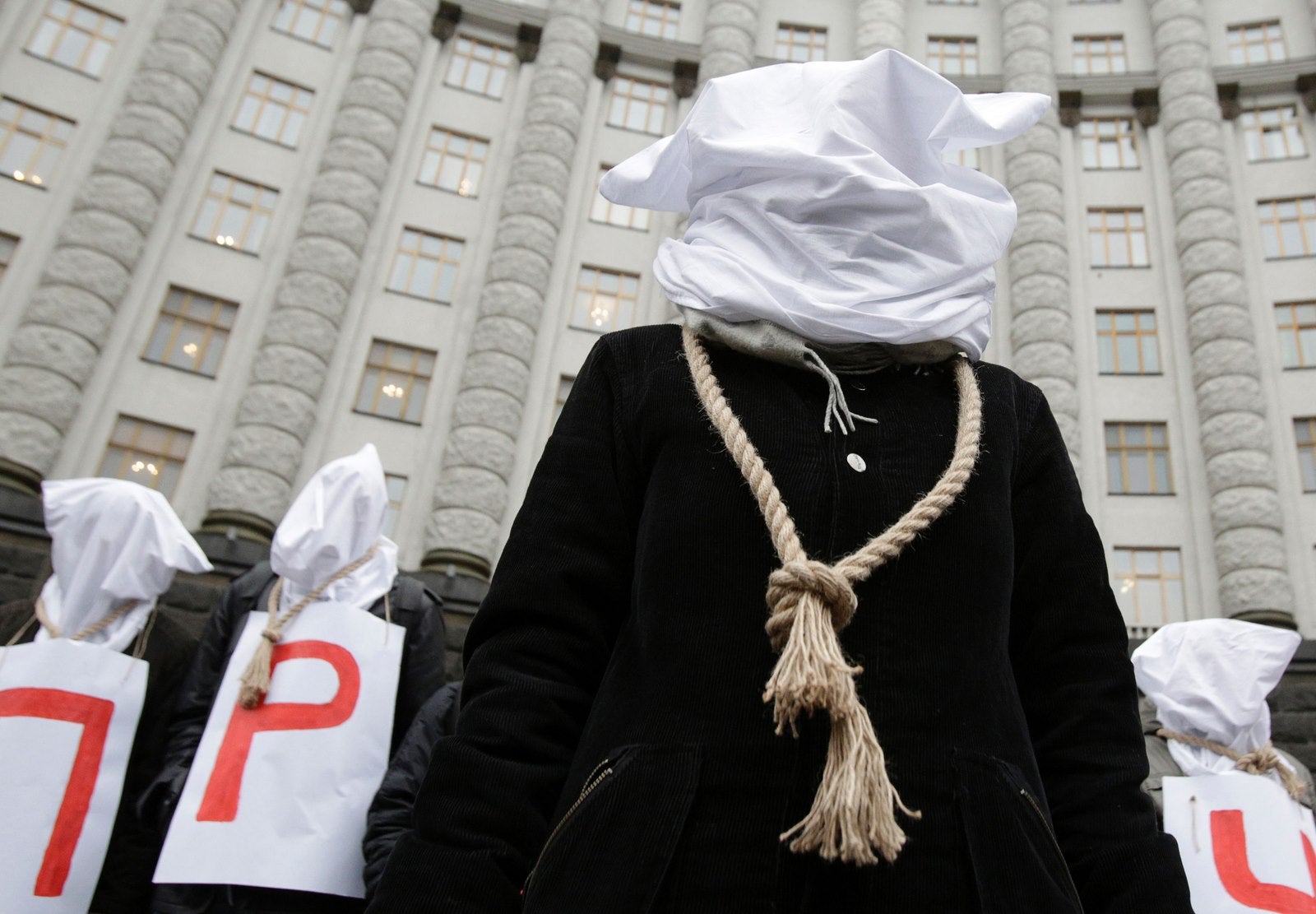 Con la cabeza cubierta y una soga alrededor del cuello protestan frente al edificio del gobierno de Ucrania en Kiev.