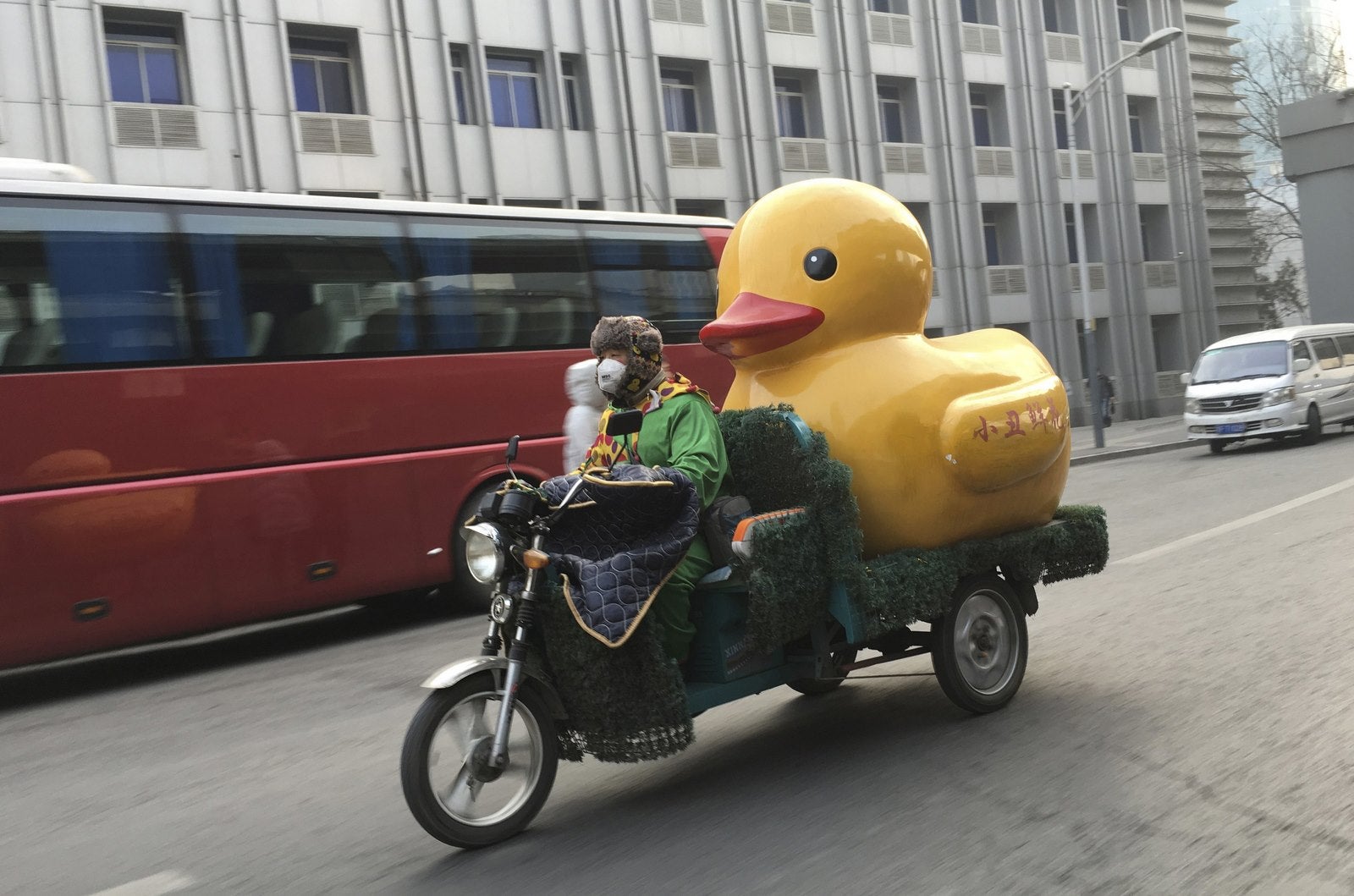 Un hombre monta un triciclo eléctrico con un pato de goma en medio de la niebla con humo pesada en Beijing, China.