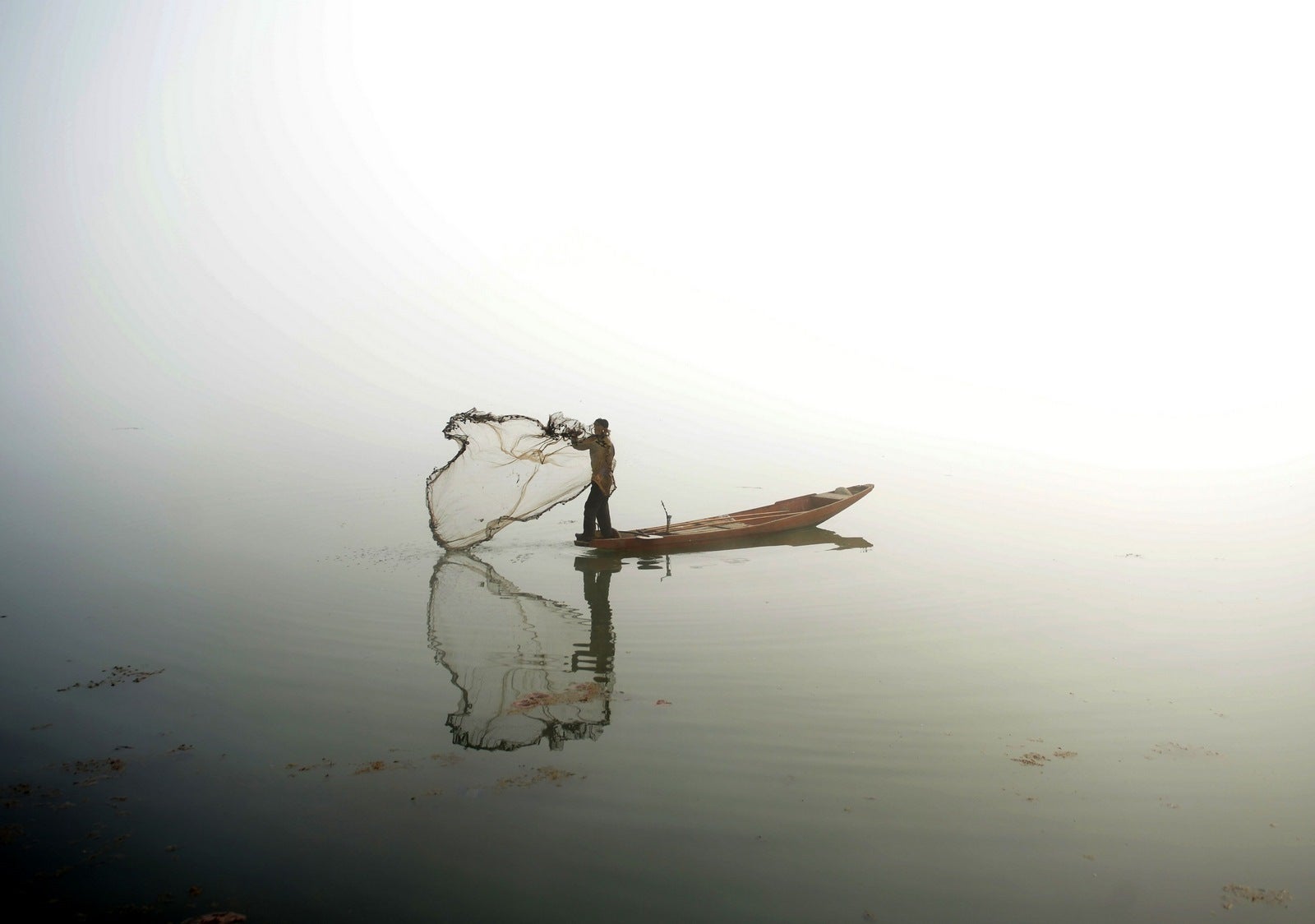 Un pescador de Cachemira lanza su red de su barco en el lago Dal durante densa niebla en Srinagar.