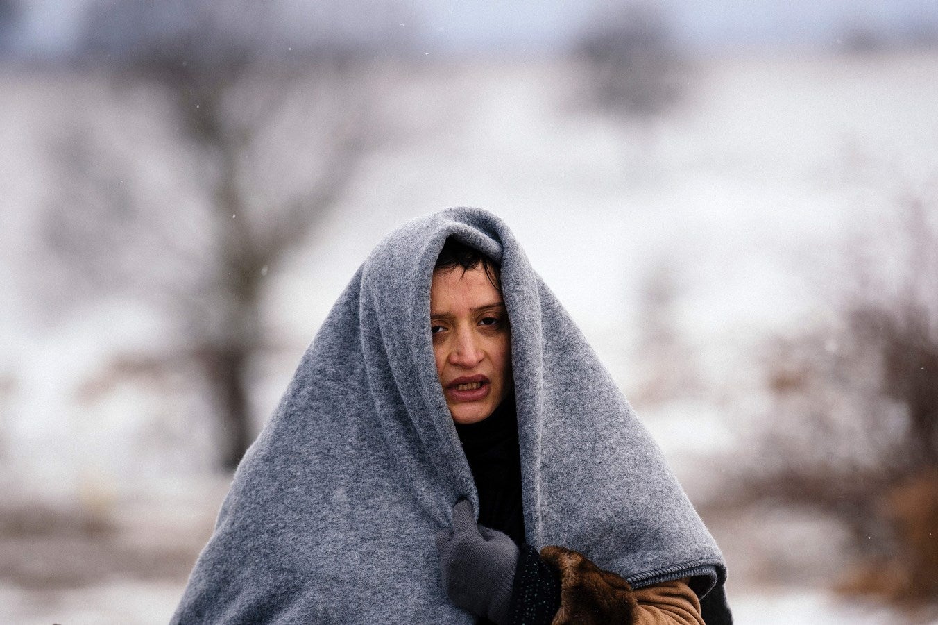 Una mujer utiliza una manta para mantener el calor mientras camina con otros inmigrantes y refugiados a través de un campo cubierto de nieve después de cruzar la frontera entre Macedonia serbia cerca del pueblo de Miratovac