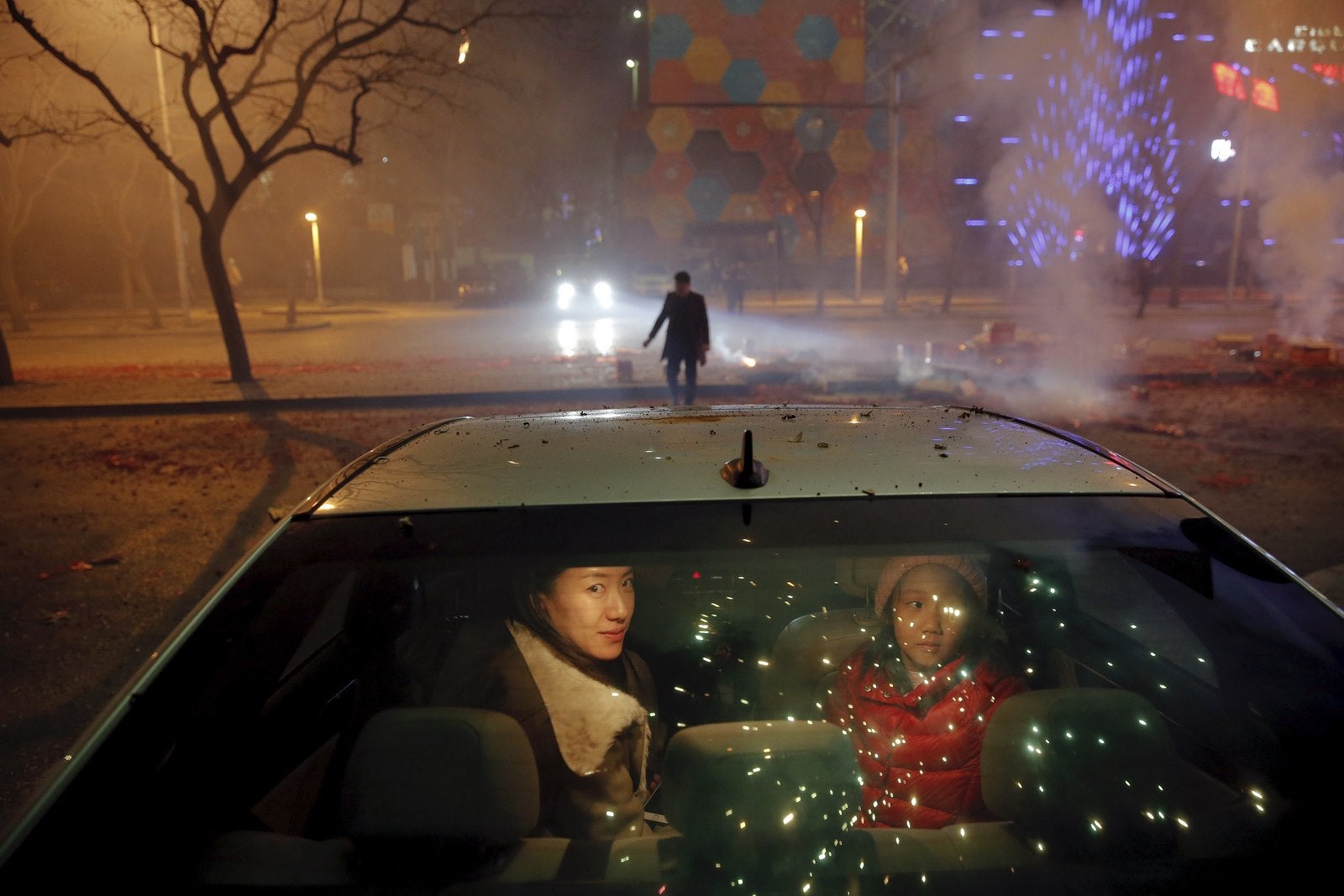 Una niña y una mujer se sientan en el interior del coche y ven como petardos y fuegos artificiales estallan celebrar el comienzo del Año Nuevo Lunar chino del mono en Beijing.