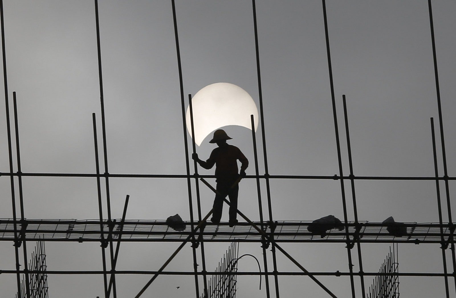 Un eclipse solar parcial se ve como un obrero trabaja en una obra de construcción en Phnom Penh, Camboya.