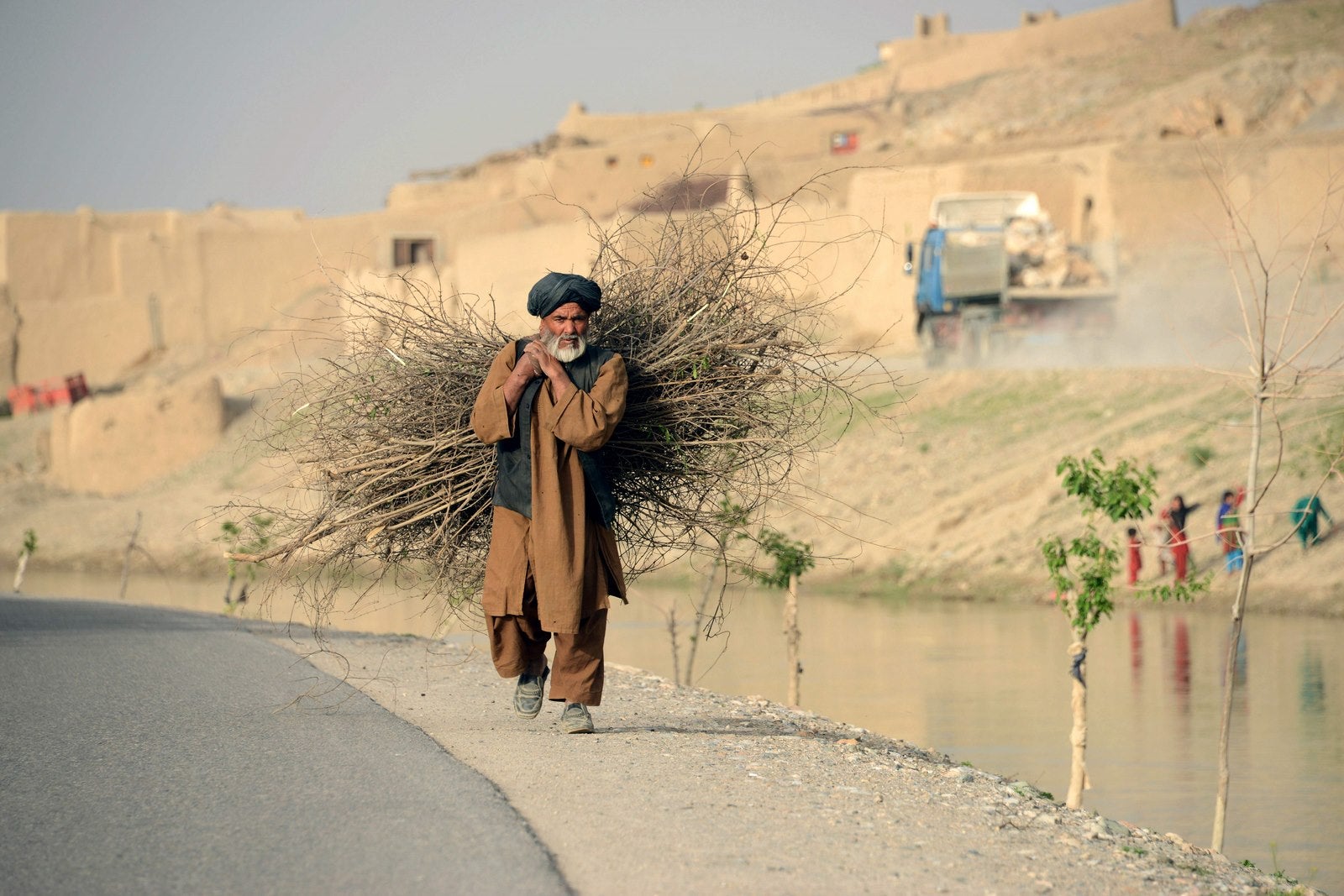 Un hombre afgano lleva leña al hombro caminando por una carretera en Kandahar.