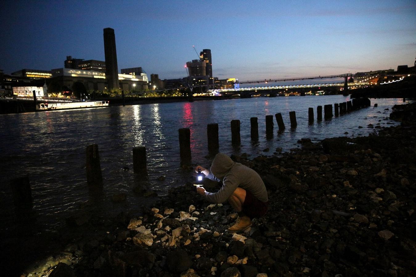 Un mudlark utiliza una linterna para buscar elementos en la orilla del río Támesis en Londres, Gran Bretaña