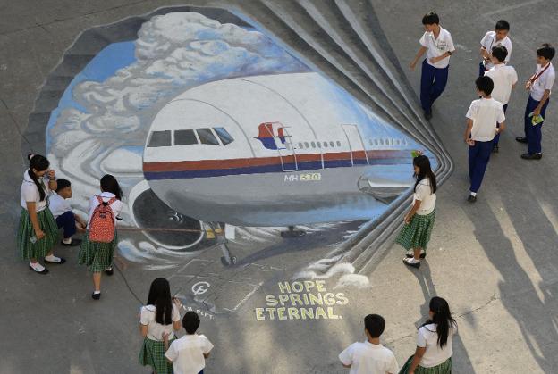 Un grupo de escolares filipinos observa un enorme mural del vuelo MH370 pintado en el suelo del colegio.