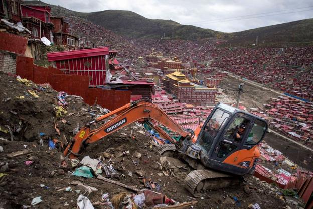 Una excavadora derriba una barriada de chabolas en el extrarradio de una ciudad china. Abajo, los escombros de un asentamiento de inmigrantes.