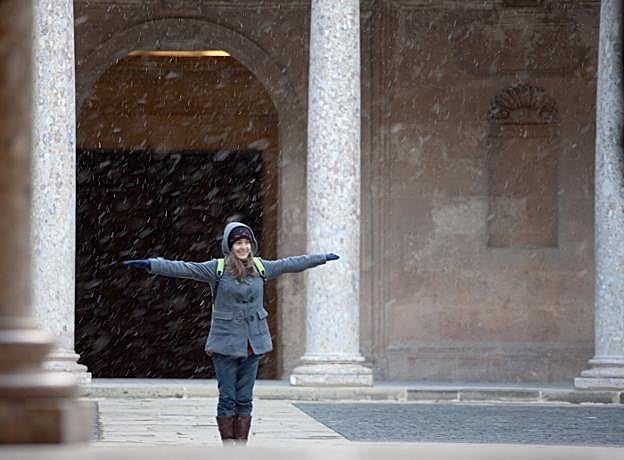 Una turista en el Palacio de Carlos V mientras una fina lluvia de copos de nieve cae sobre el monumento.