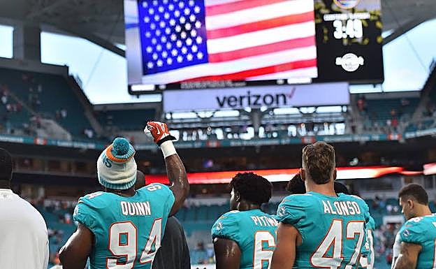 Jugadores de los Dolphins de Miami levantan el puño al sonar el himno en el estadio. 