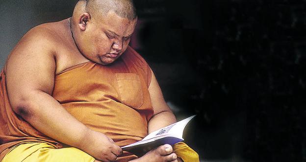 Un monje tailandés con evidente sobrepeso se dedica a la meditación a través de la lectura.