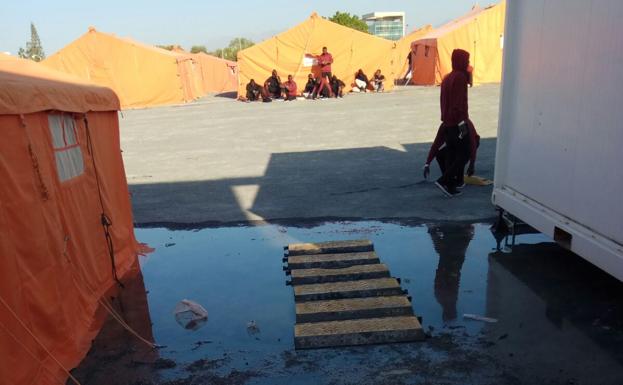 Inmigrantes en el campamento del puerto de Motril con un charco, que según el SUP, procede del desborde aguas fecales.