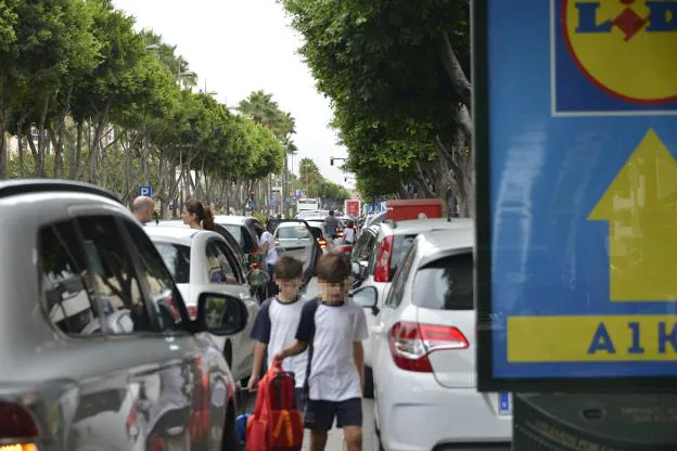 Dos pequeños avanzan entre la doble fila de coches en la avenida Federico García Lorca. 