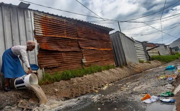 Una mujer tira agua sucia en un canal contaminado situado junto a una fuente pública de agua potable en Ciudad del Cabo (Sudáfrica).
