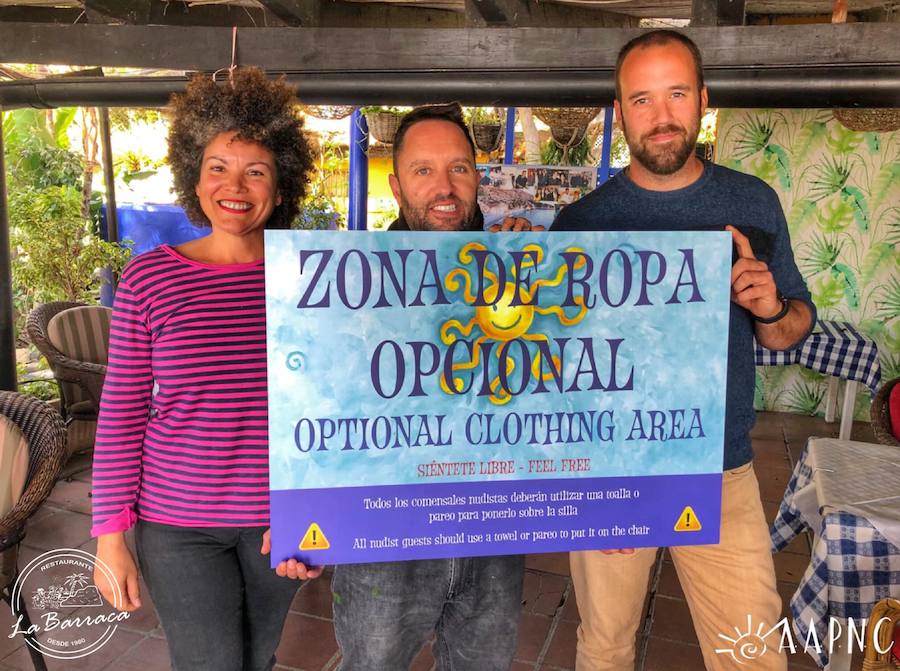 El propietario de La Barraca, entre el presidente y una directiva de la Asociación de amigos de la playa naturista de Cantarriján, con el cartel que acotará la zona para los clientes sin ropa. 