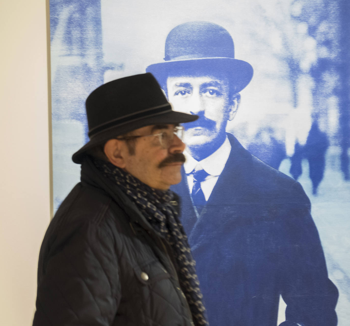 Un hombre con sombrero y bigote pasa por delante de Falla, también con sombrero y bigote, en la exposición del Zaida.