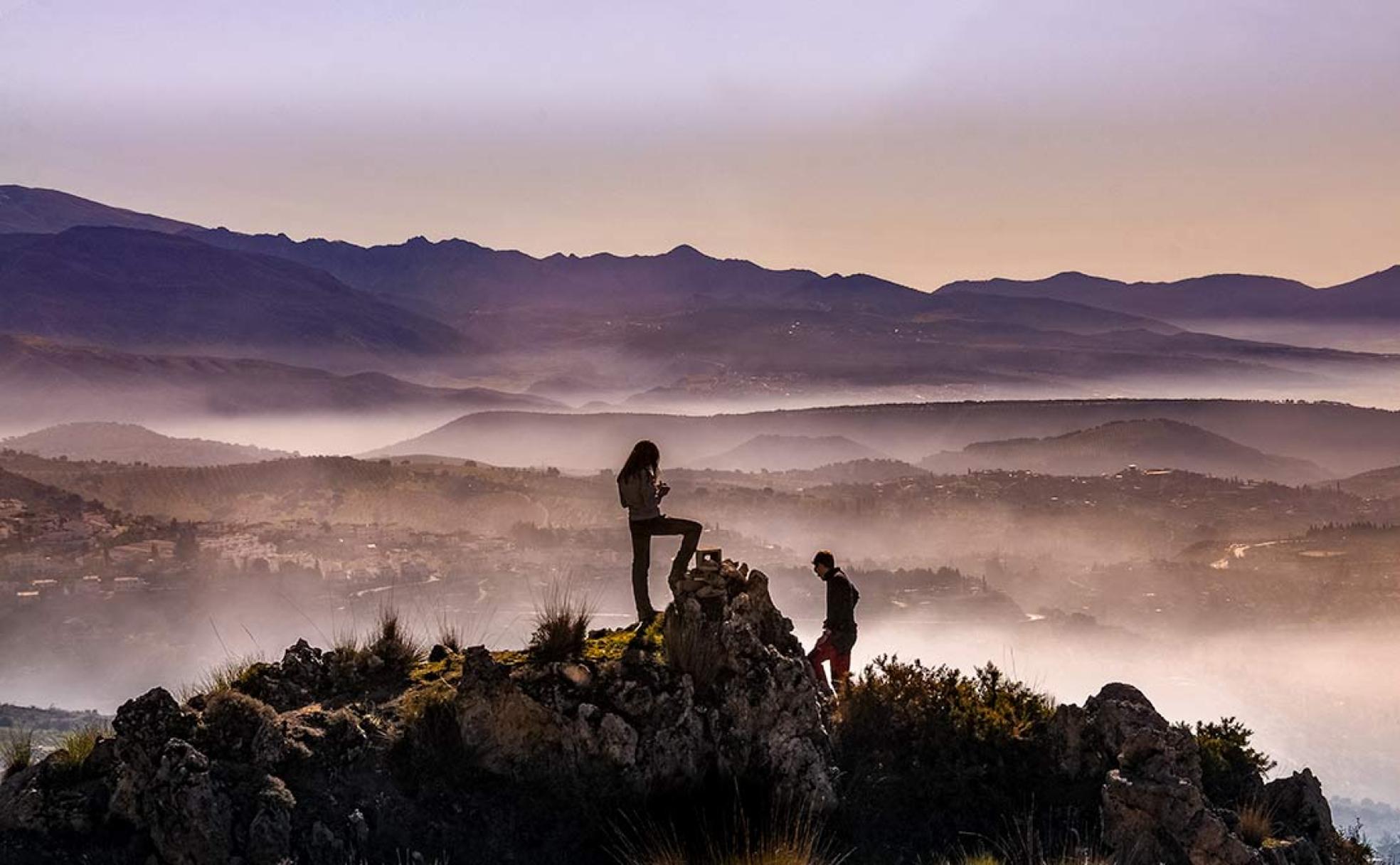 Una pareja contempla el valle de Granada desde los picachos previos a la Alfaguara 