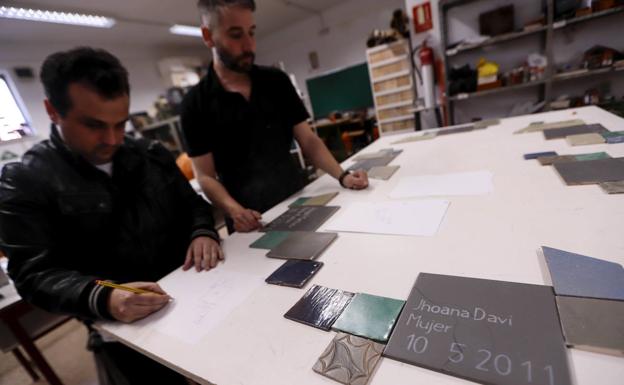 El profesor Juanma Herrera, junto a uno de sus alumnos, muestra algunos de los diseños de las lápidas.