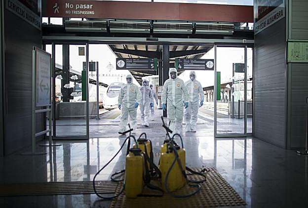 Miembros de la UME, protegidos con un traje de aislamiento, caminan hacia las mochilas con las que desinfectaron la estación.