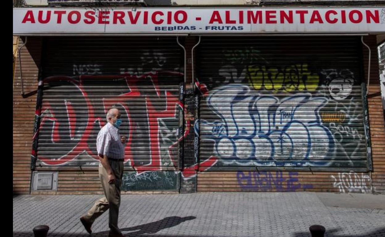 Un hombre protegido con mascarilla camina ante un comercio cerrado.