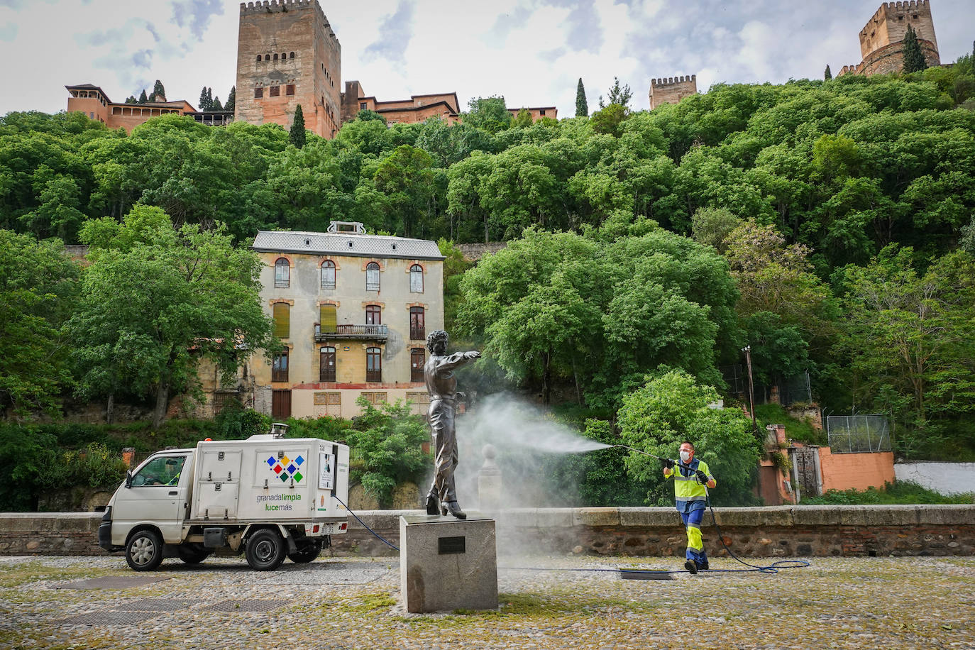 Operarios de Inagra desinfectan el Paseo de los Tristes, con la Alhambra como telón de fondo.