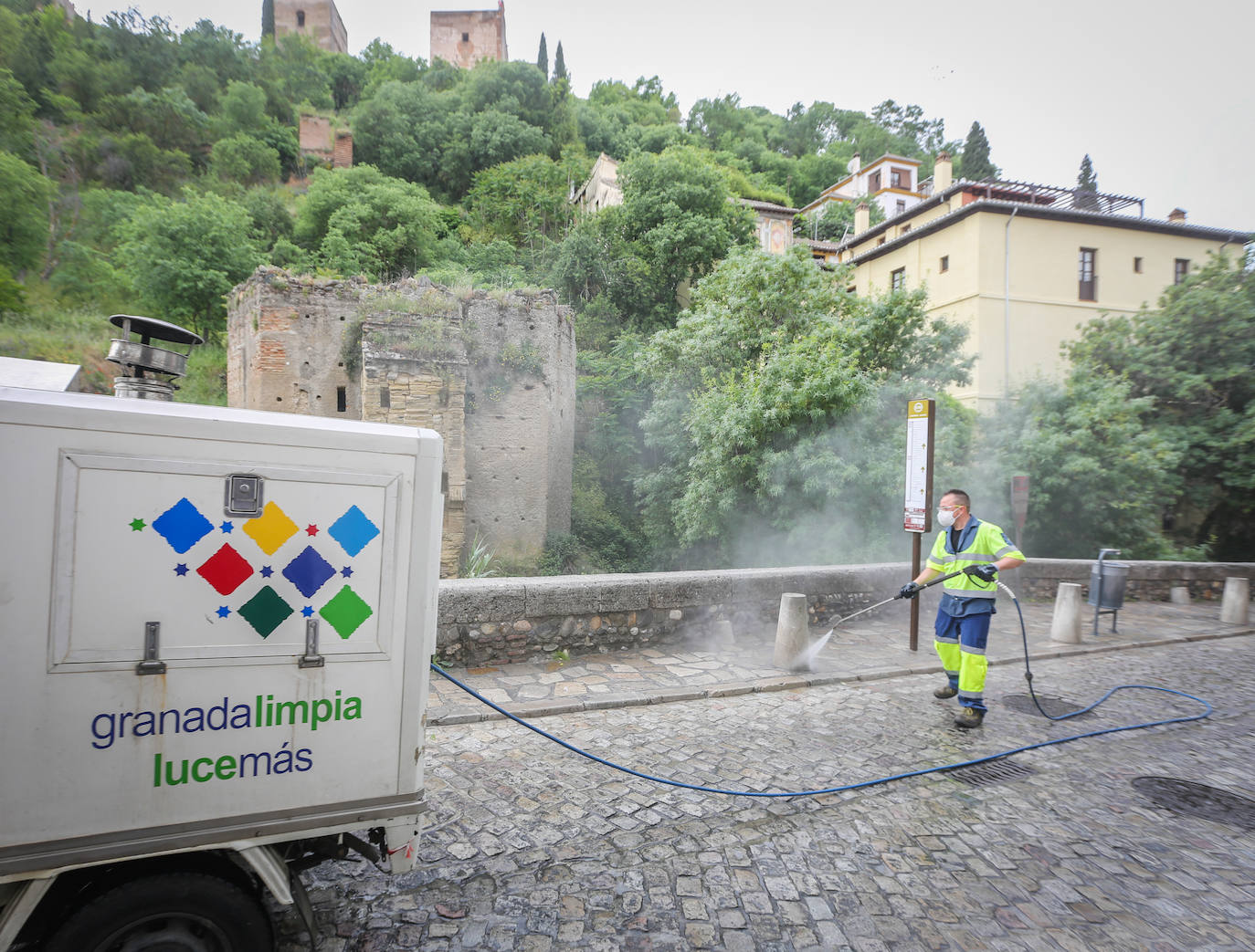 Operarios de Inagra desinfectan el Paseo de los Tristes, con la Alhambra como telón de fondo.