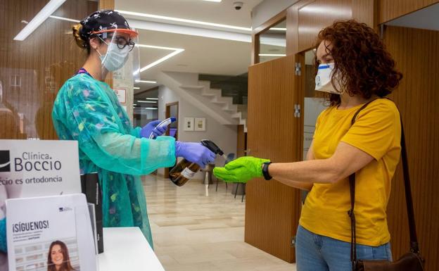 Una auxiliar desinfecta las manos y mide la temperatura corporal de una paciente en la entrada a una clínica dental de Huelva.