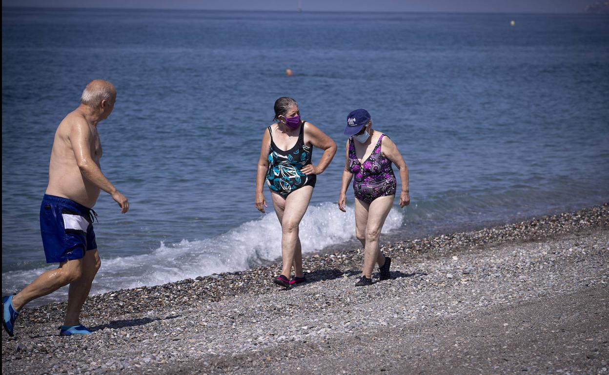 Dos bañistas pasean por la orilla con sus mascarillas puestas.