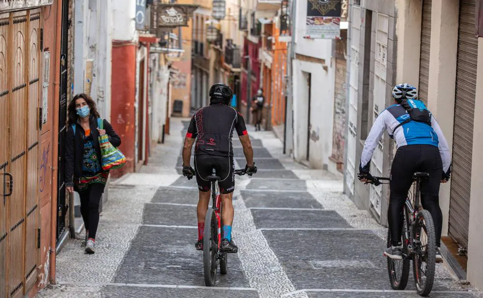 Dos ciclistas bajan montados por en medio de la calle Calderería, una de las principales arterias del barrio del Albaicín.