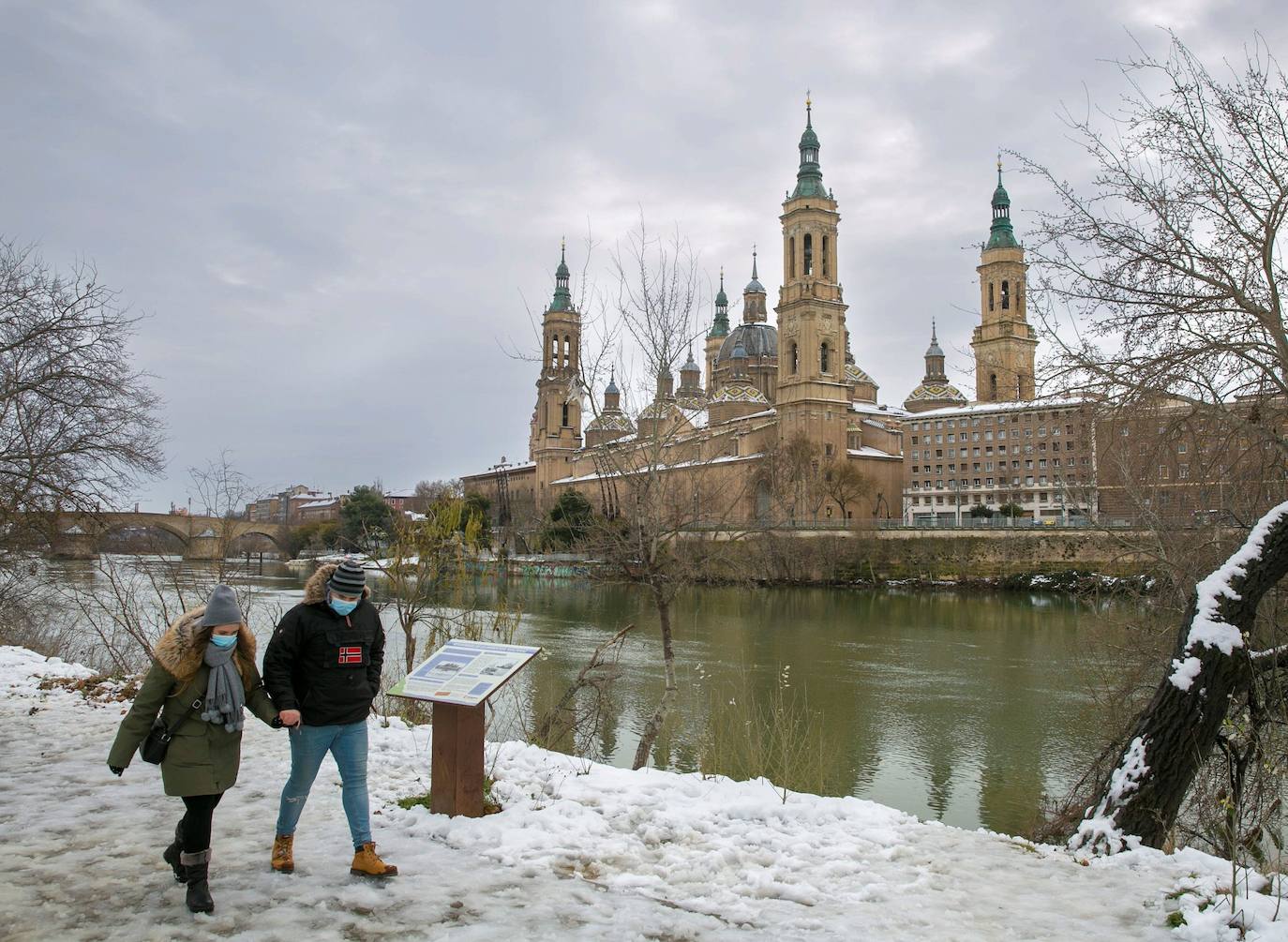 Unos paseantes caminan por la nieve ante la Basílica del Pilar de Zaragoza, este domingo