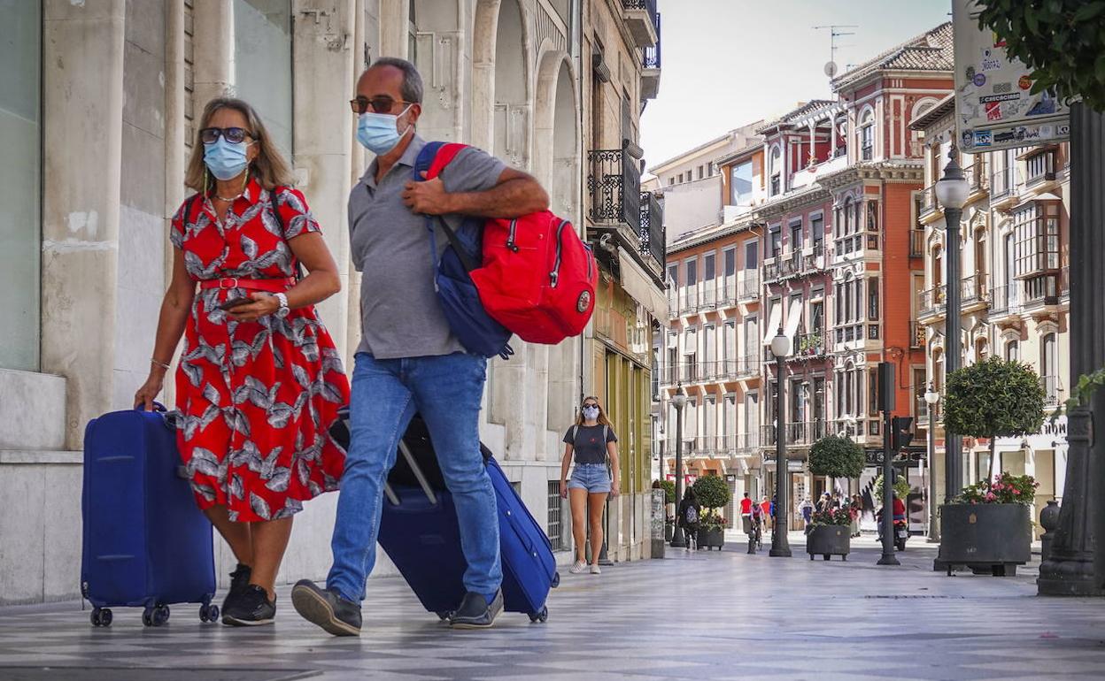 Dos turistas pasean con mascarilla por una céntrica calle de la capital granadina. 