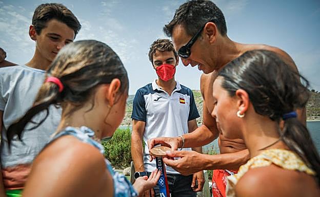 Imagen principal - Arriba, Jordi Xammar muestra su medalla a otros aficionados a navegar en Rules. Abajo a la izquierda, el barcelonés pasea junto a su prometida Carmen y su perro Bombo. A la izquierda, emerge de Rules con la medalla en la mano. 