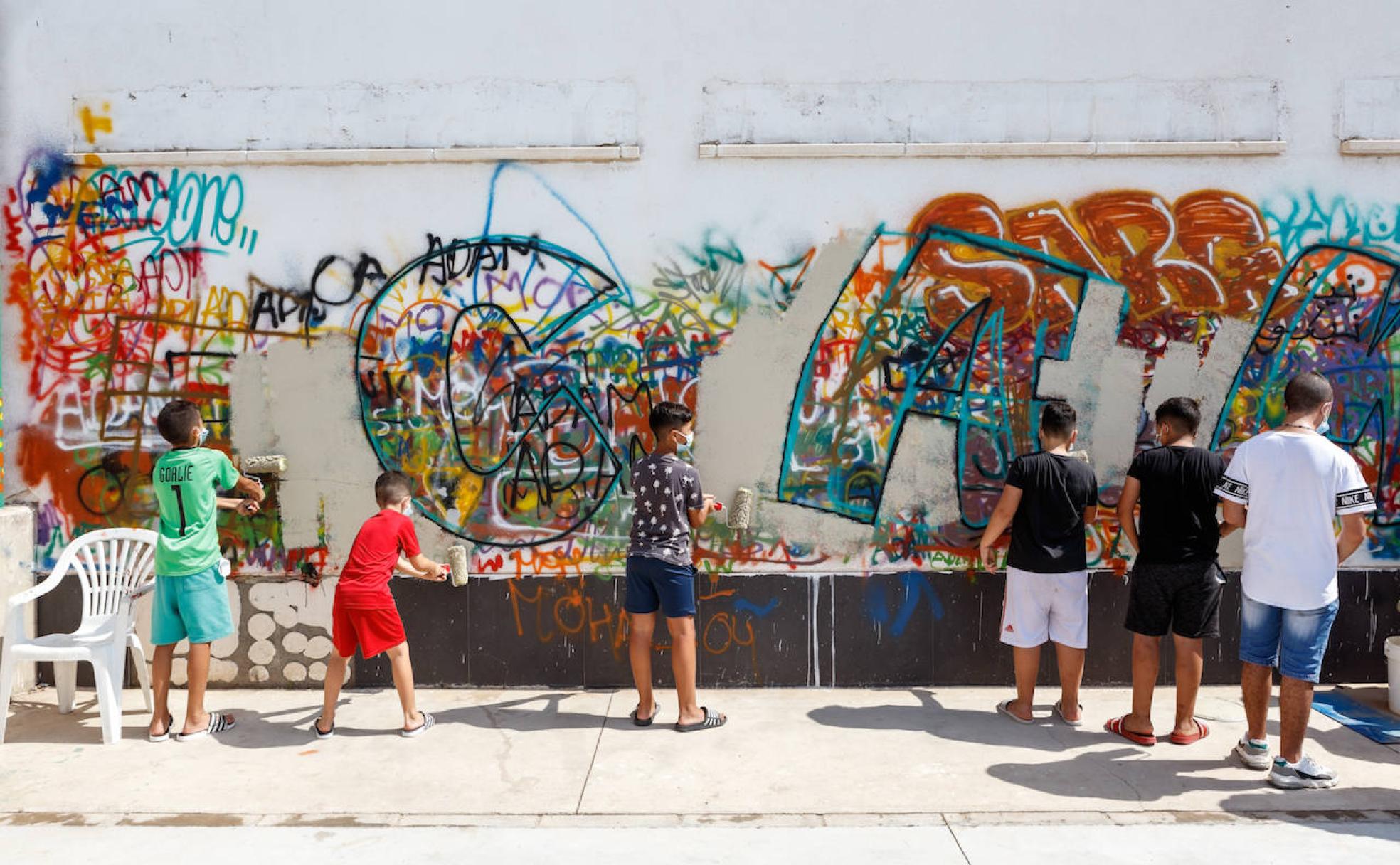 Jóvenes pintando una pared en el Puche en la que se realizó un mural con la palabra 'Cambio'.