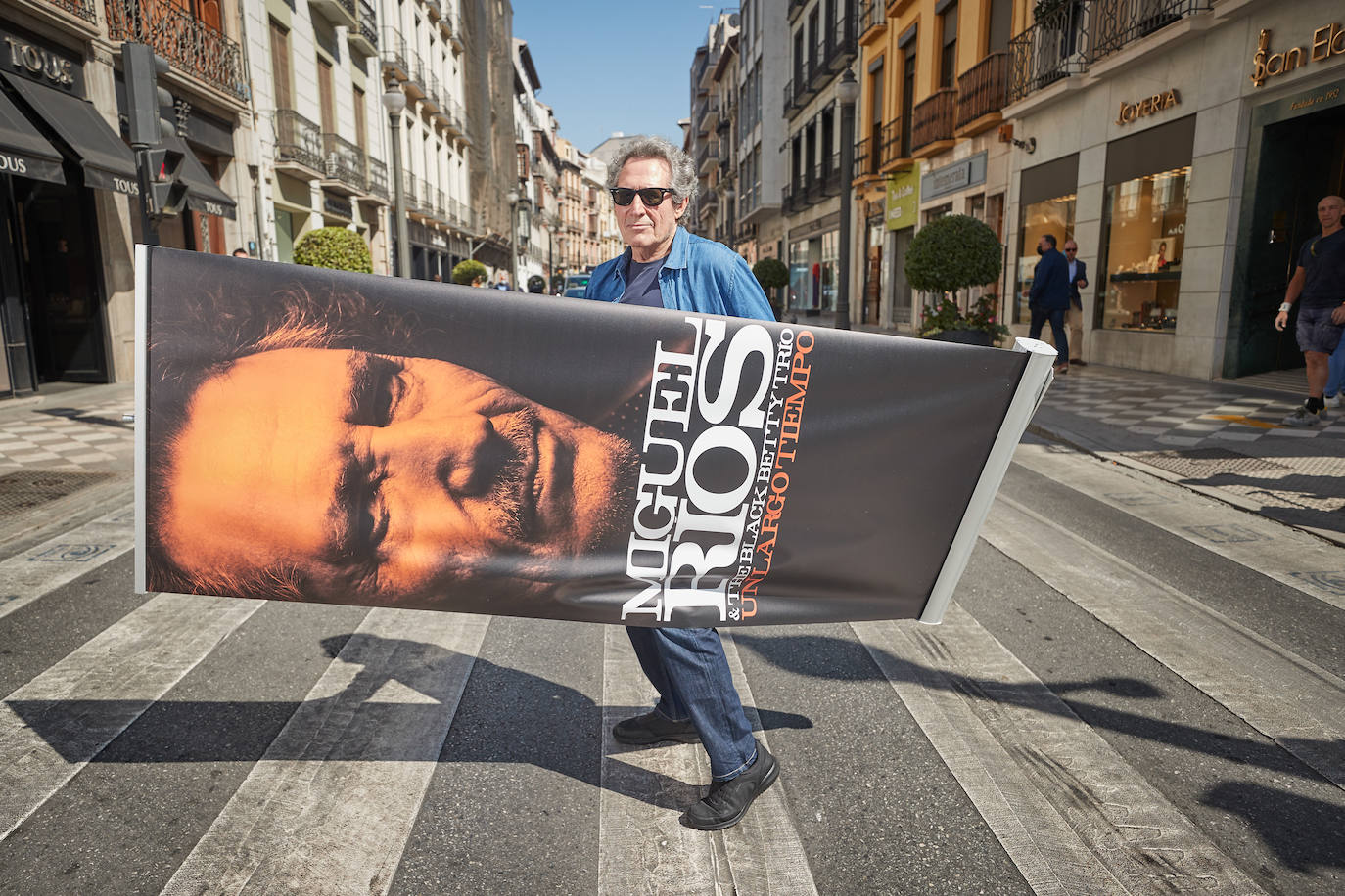Miguel Ríos cruza la calle Reyes Católicos de Granada con un cartel de presentación de su concierto.
