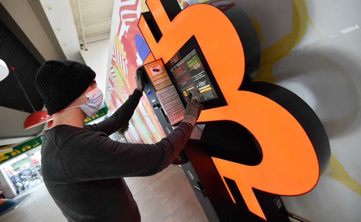 Un joven se interesa por un cajero que permite adquirir Bitcoin en un centro comercial. 