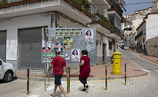 Dos vecinos pasan delante de un panel con propaganda en la calle Rosario de Salobreña.