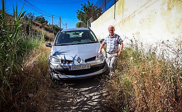 José Heredia, junto a su coche, rodeado de toda la maleza que ha invadido su camino a casa. 