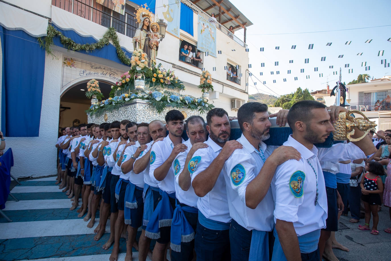 La Virgen del Carmen de Almuñéca, con el Barrio de Los Marinos al fondo, enfila la playa de San Cristóbal tras salir de la capilla.