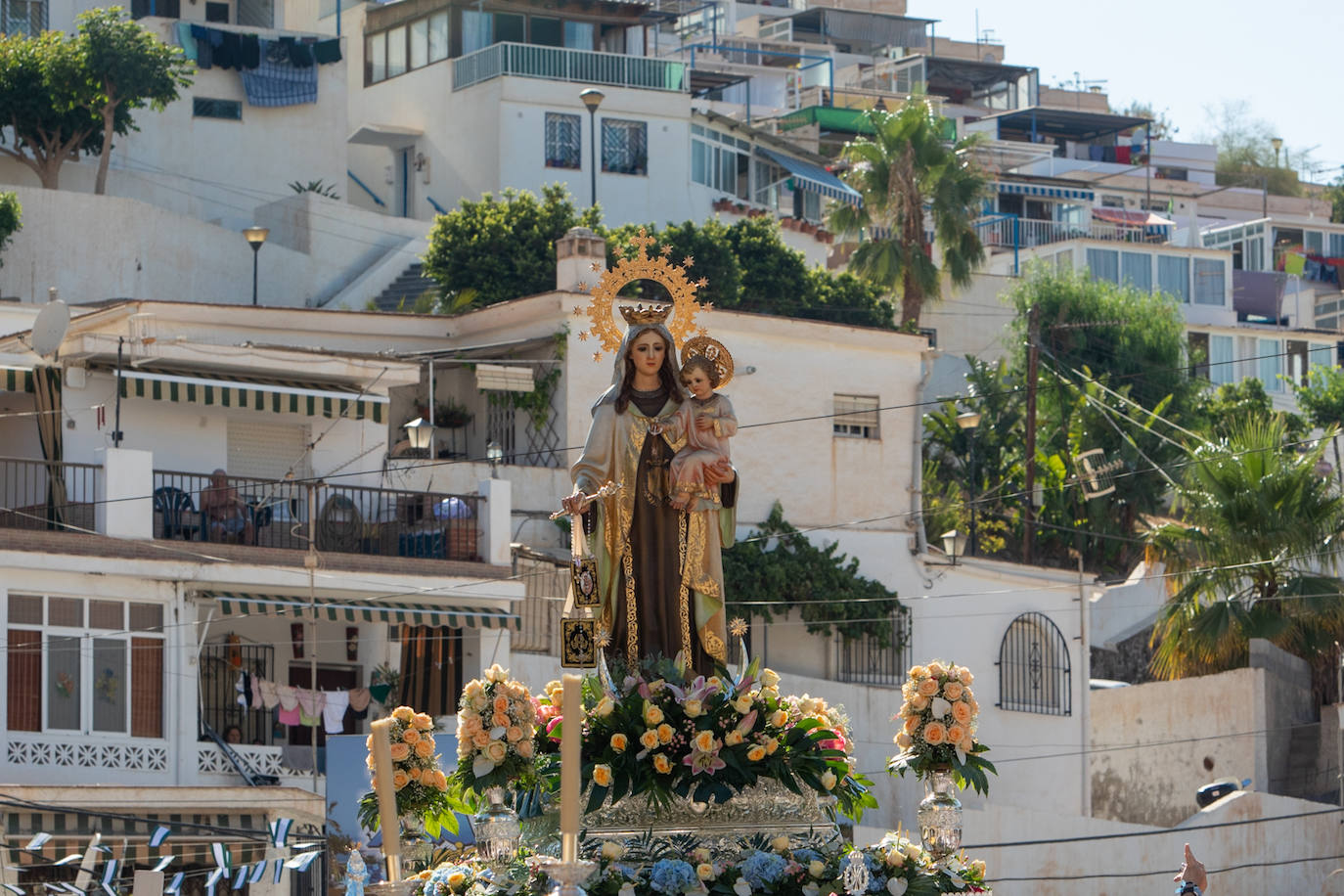 La Virgen del Carmen de Almuñéca, con el Barrio de Los Marinos al fondo, enfila la playa de San Cristóbal tras salir de la capilla.