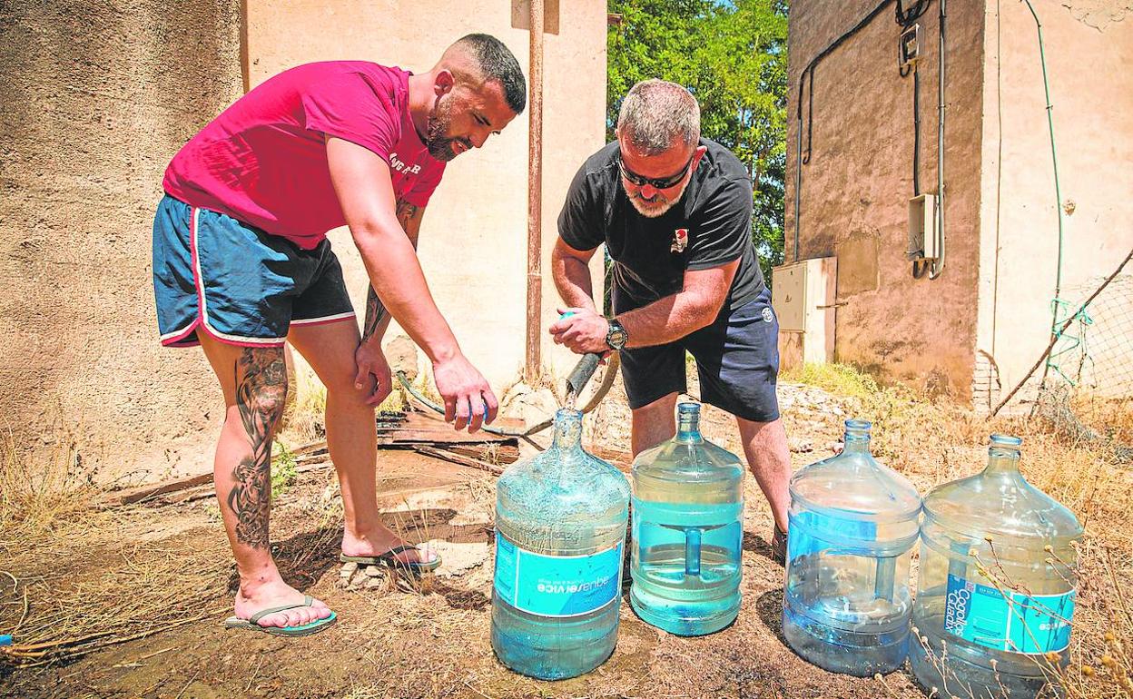 Dos afectados llenan garrafas para hacer frente al corte y la ola de calor. 