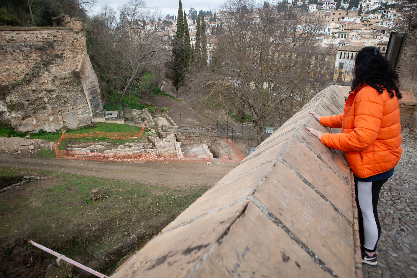 Una mujer se asoma al tapial para observar los restos encontrados en las excavaciones.