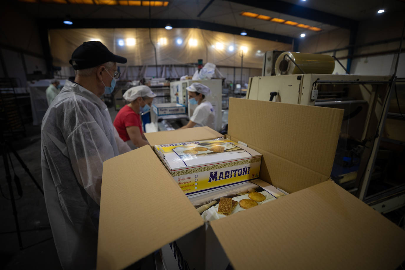 Imagen secundaria 2 - Mari Toñi Pérez posando con una caja de sus tortas y trabajadores en el obrador.