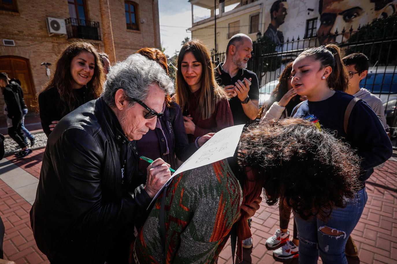 Miguel Ríos firma un autógrafo apoyándose en la espalda de una profesora.