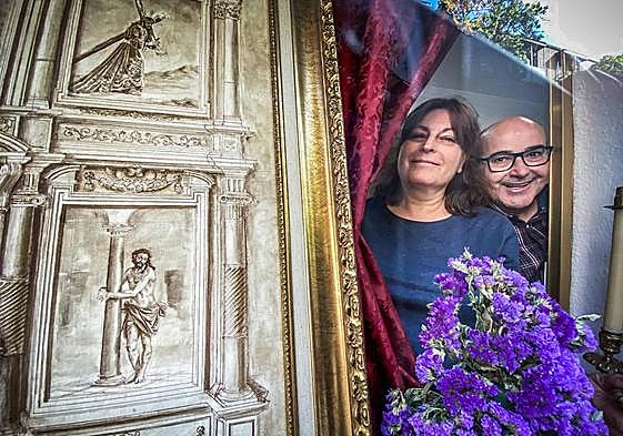 Paco Cordones y Encarni miran a través de la ventana de su cafetería en la calle Molinos, cuyo escaparate está adornado para la Semana Santa.