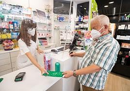 Un hombre compra en una farmacia con mascarilla.