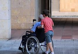 Un niño empuja la silla de rueda de un mayor dependiente.