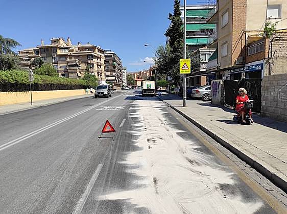La máquina averiada (al fondo) y el reguero de aceite ya cubierto de material antideslizante en la avenida de Dilar.
